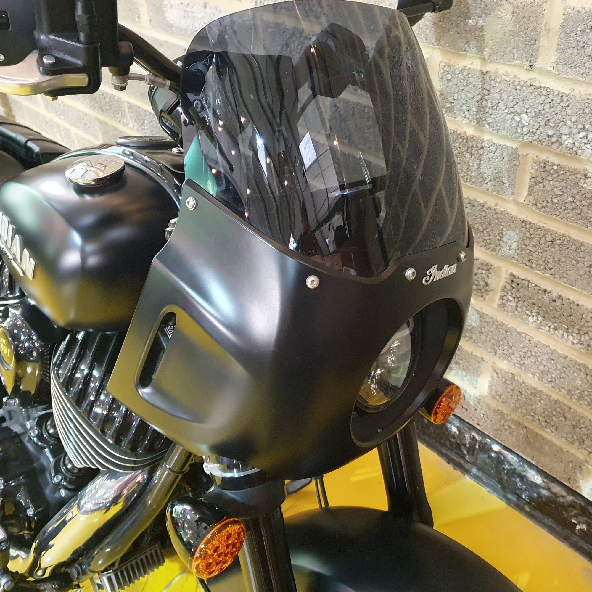 Close-up of a motorcycle's front section with a black windshield against a brick wall.