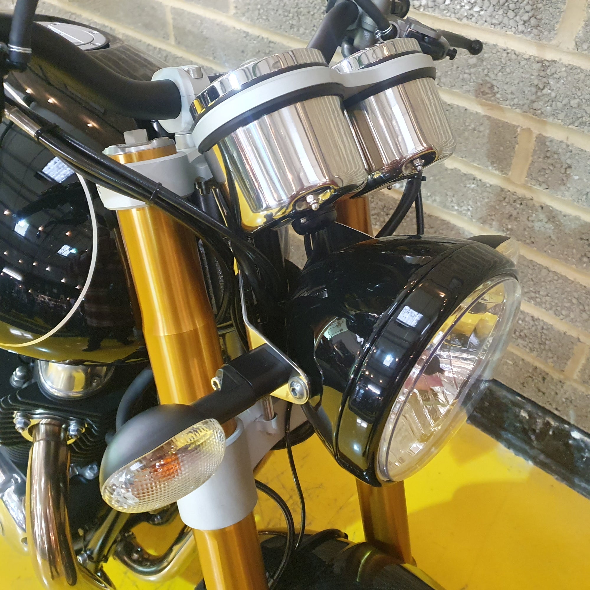 Close-up of a motorcycle's headlight and handlebars against a brick wall.