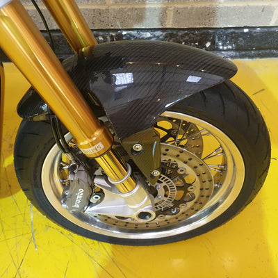 Close-up of a motorcycle wheel with gold suspension fork on a yellow background