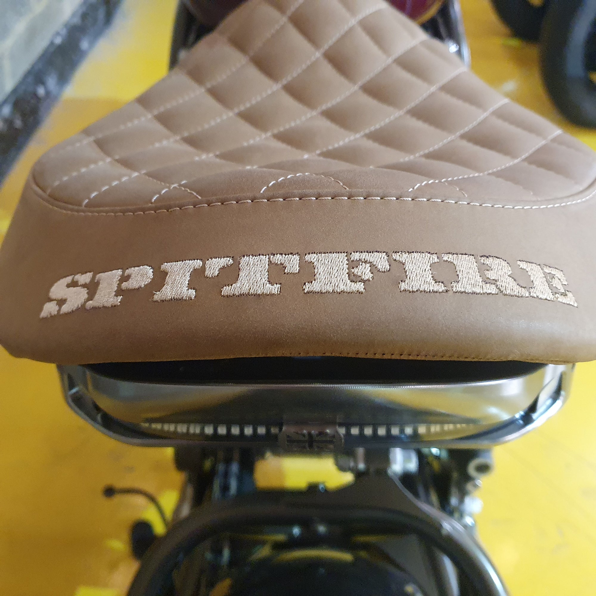 Brown quilted motorcycle seat with 'SPITFIRE' branding on a yellow background