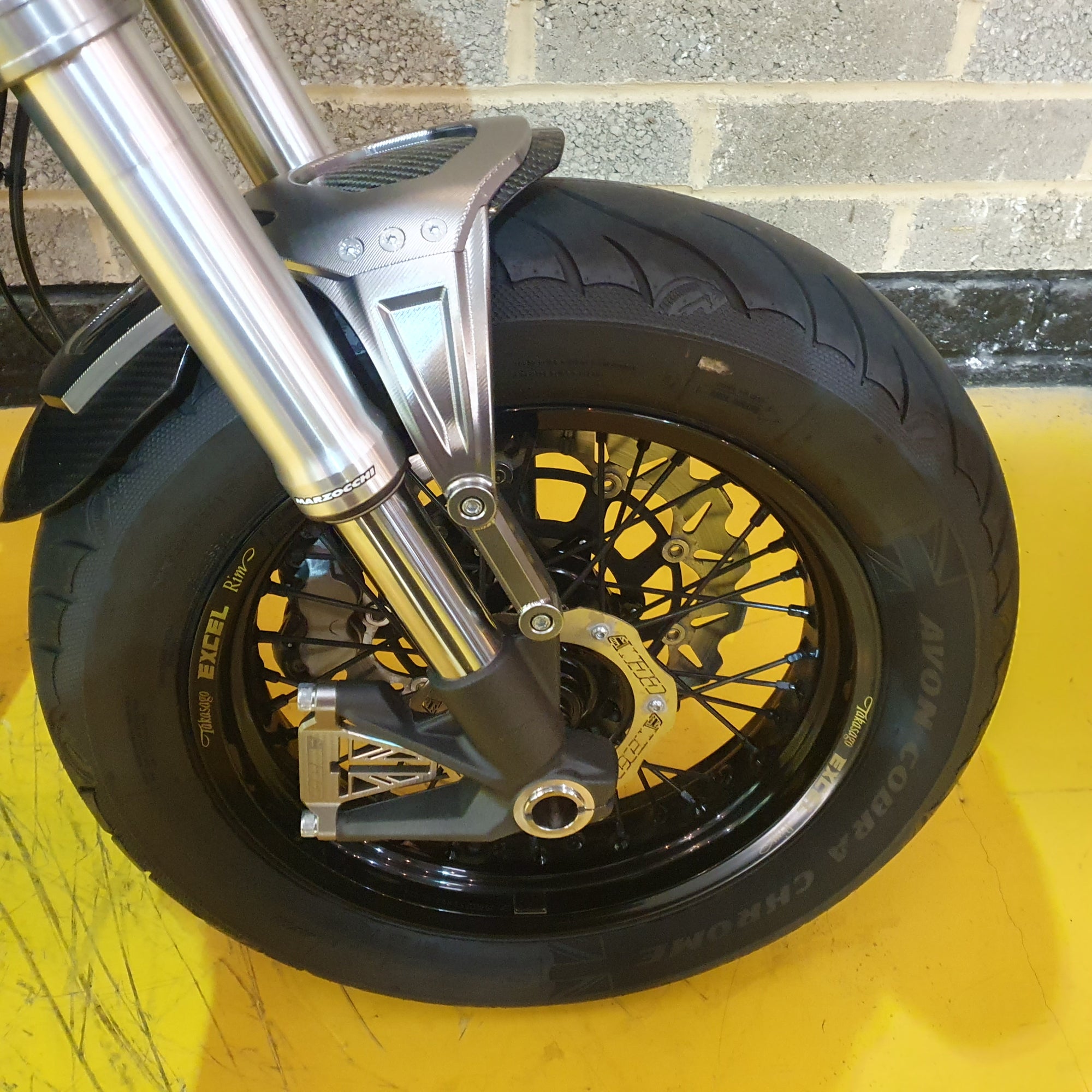 Close-up of a motorcycle wheel with a yellow rim and black tire against a brick wall.