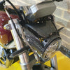 Close-up of a motorcycle headlight with carbon fiber design against a brick wall background