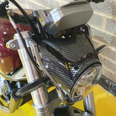 Close-up of a motorcycle headlight with carbon fiber design against a brick wall background