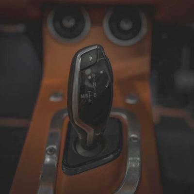 Car gear shift lever with 'P', 'R', 'N', 'D', 'L' markings on a wooden dashboard.