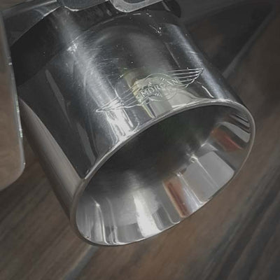 Metallic exhaust tip with a brand logo on a wooden surface