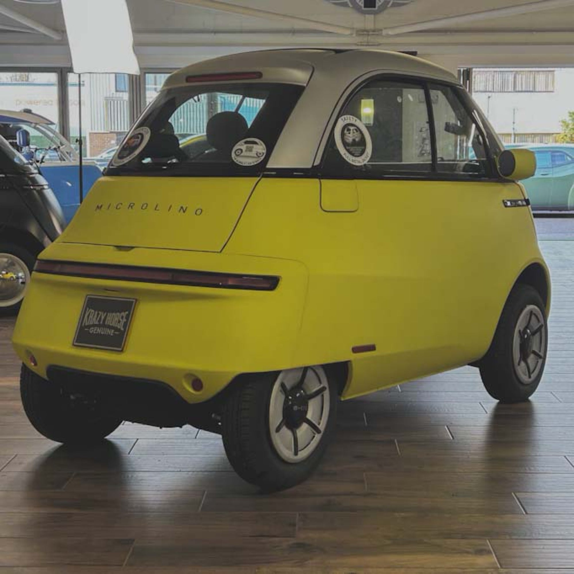 Yellow microcar with 'Microlino' branding inside a showroom.