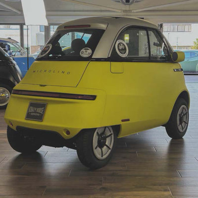 Yellow microcar with 'Microlino' branding inside a showroom.