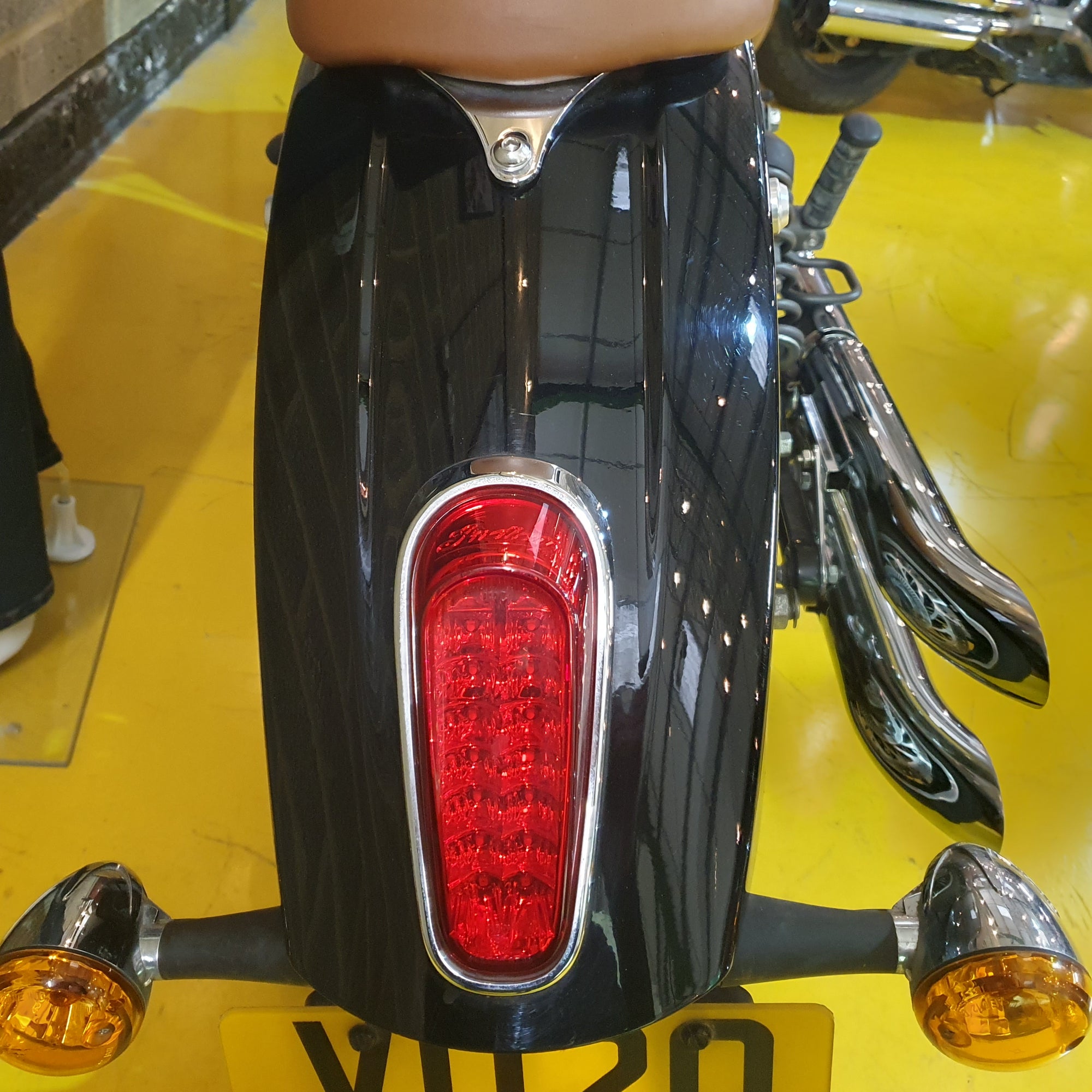 Close-up of a motorcycle's tail light and exhaust on a yellow floor.
