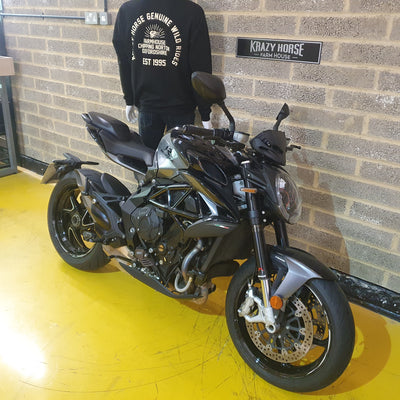 Black motorcycle parked indoors against a brick wall with 'Krazy Horse' branding.