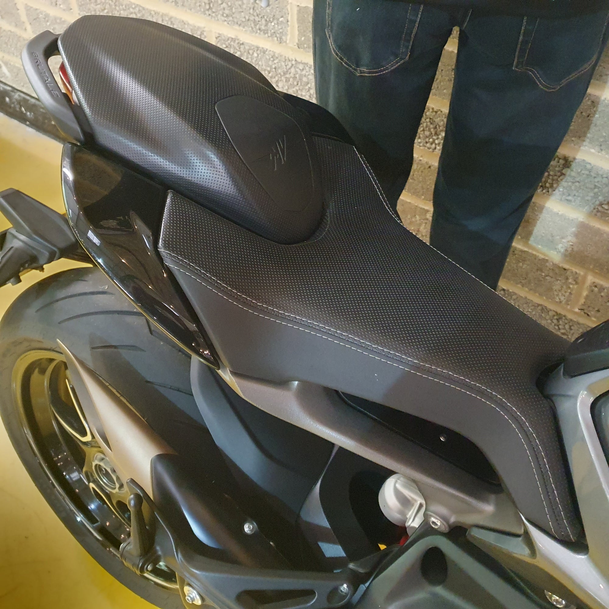 Close-up of a motorcycle seat with a person standing next to it on a brick surface.