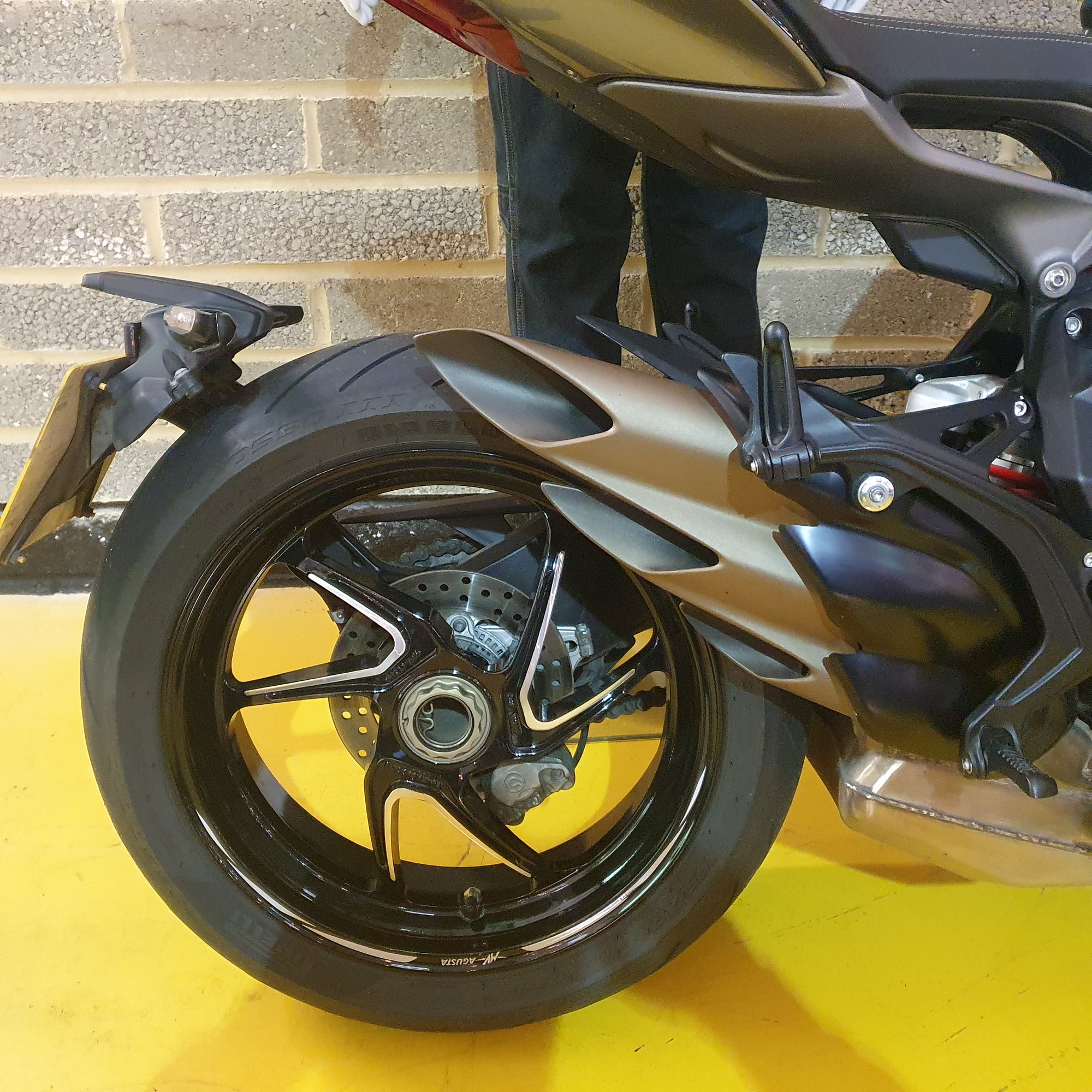 Close-up of a motorcycle wheel on a yellow surface with a brick wall background