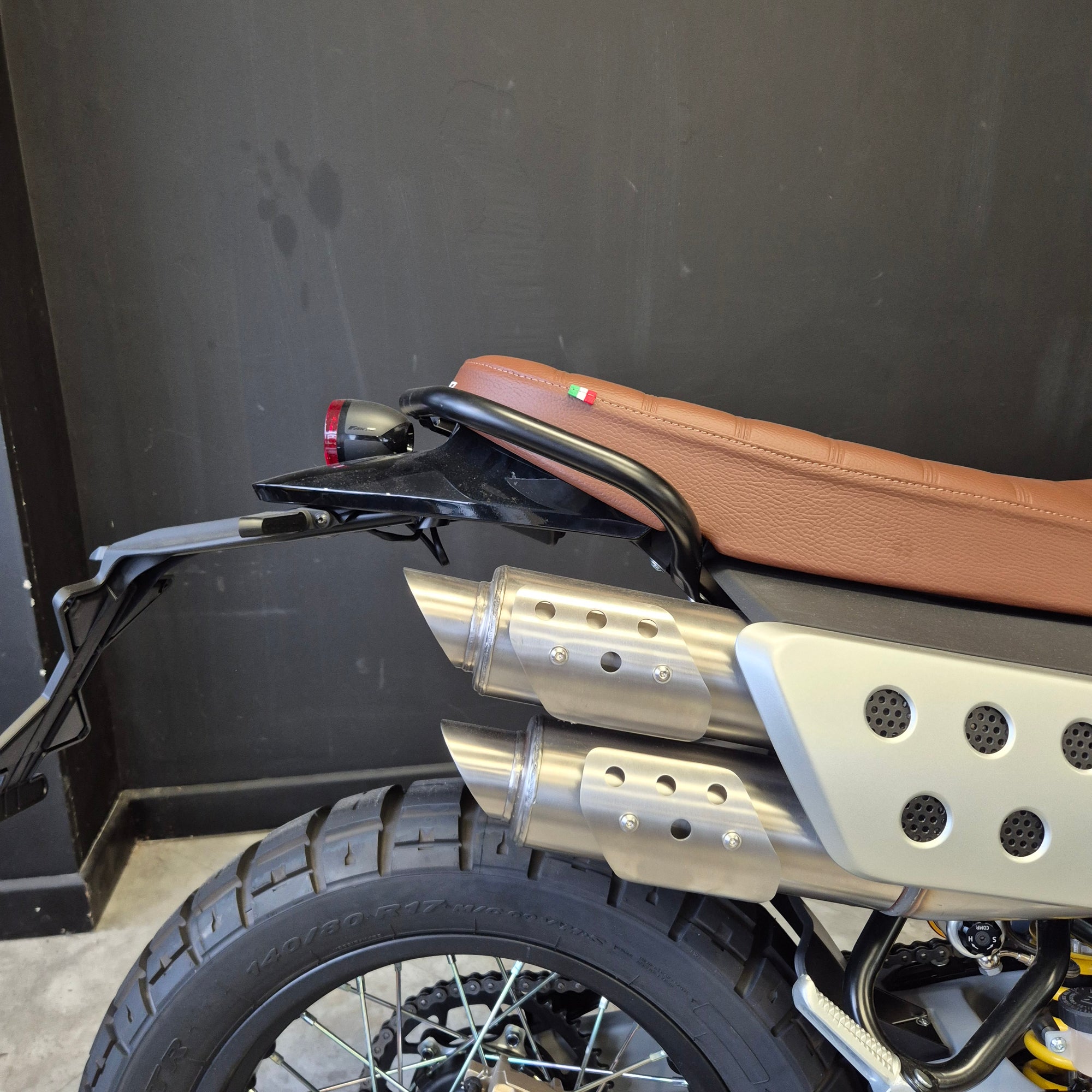 Close-up of a motorcycle exhaust system with a brown seat and black floorboard.