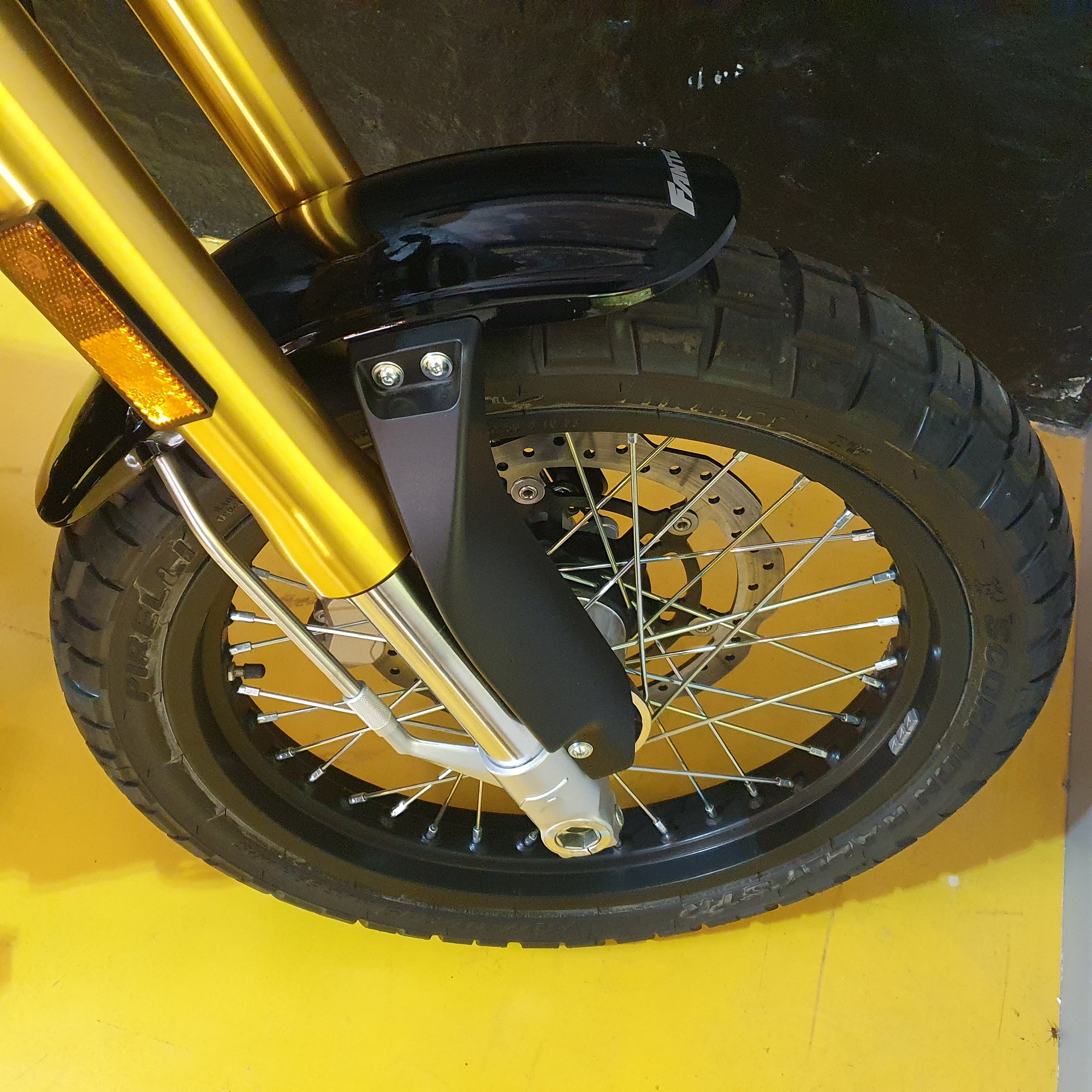 Close-up of a motorcycle wheel with gold suspension fork on a yellow background