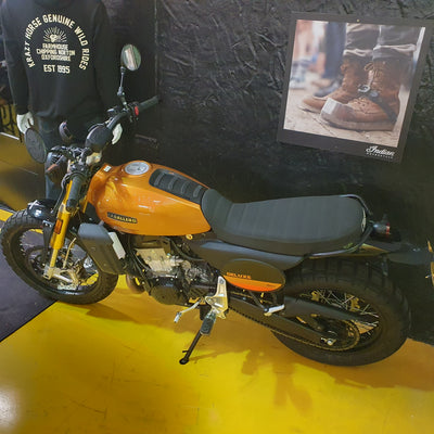 Orange and black motorcycle on a yellow floor with a dark textured wall in the background.