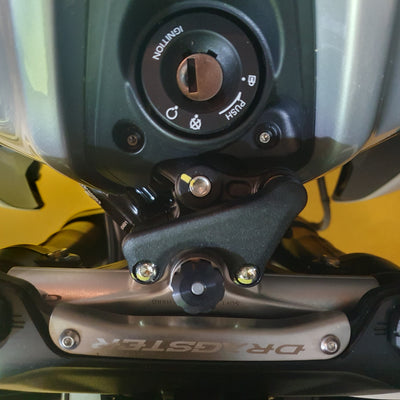 Close-up of a motorcycle fuel tank ignition switch and mounting hardware, with a silver DRAGSTER-branded metal bar visible below.