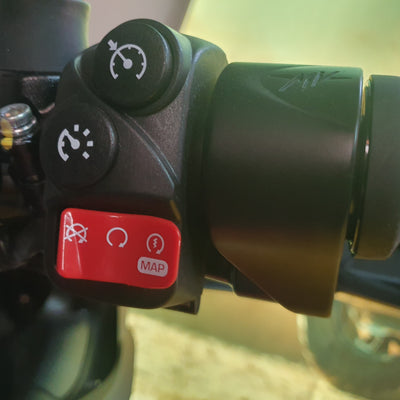 Close-up of a motorcycle handlebar control cluster with black buttons and a red MAP switch, mounted on a black handlebar.