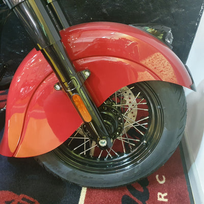 Close-up of a red motorcycle front wheel with a glossy red fender, black tire, and chrome fork, photographed indoors on a patterned rug.