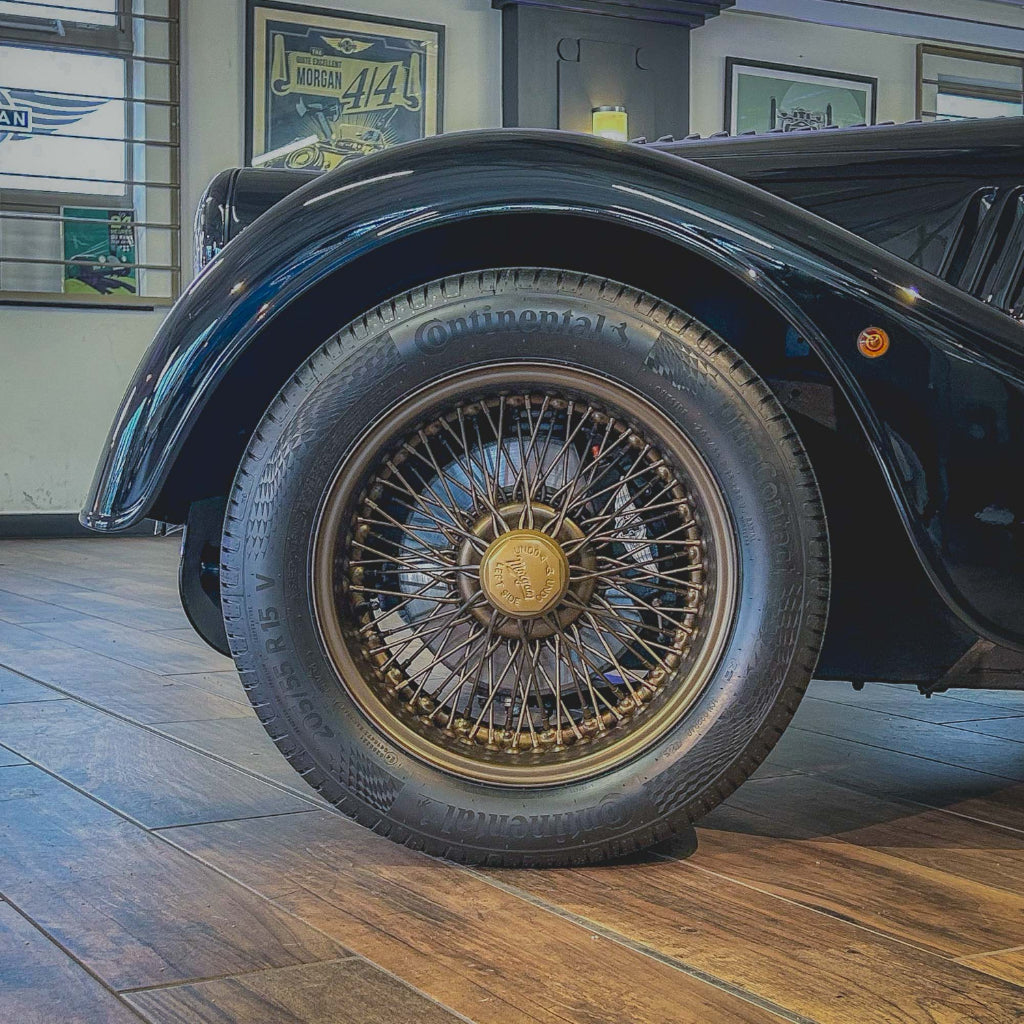 Close-up of a vintage car's wheel with a wooden floor and framed pictures in the background