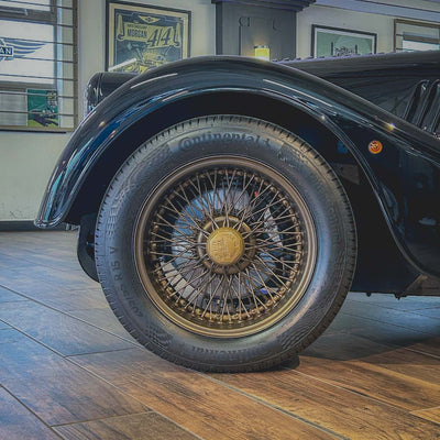 Close-up of a vintage car's wheel with a wooden floor and framed pictures in the background