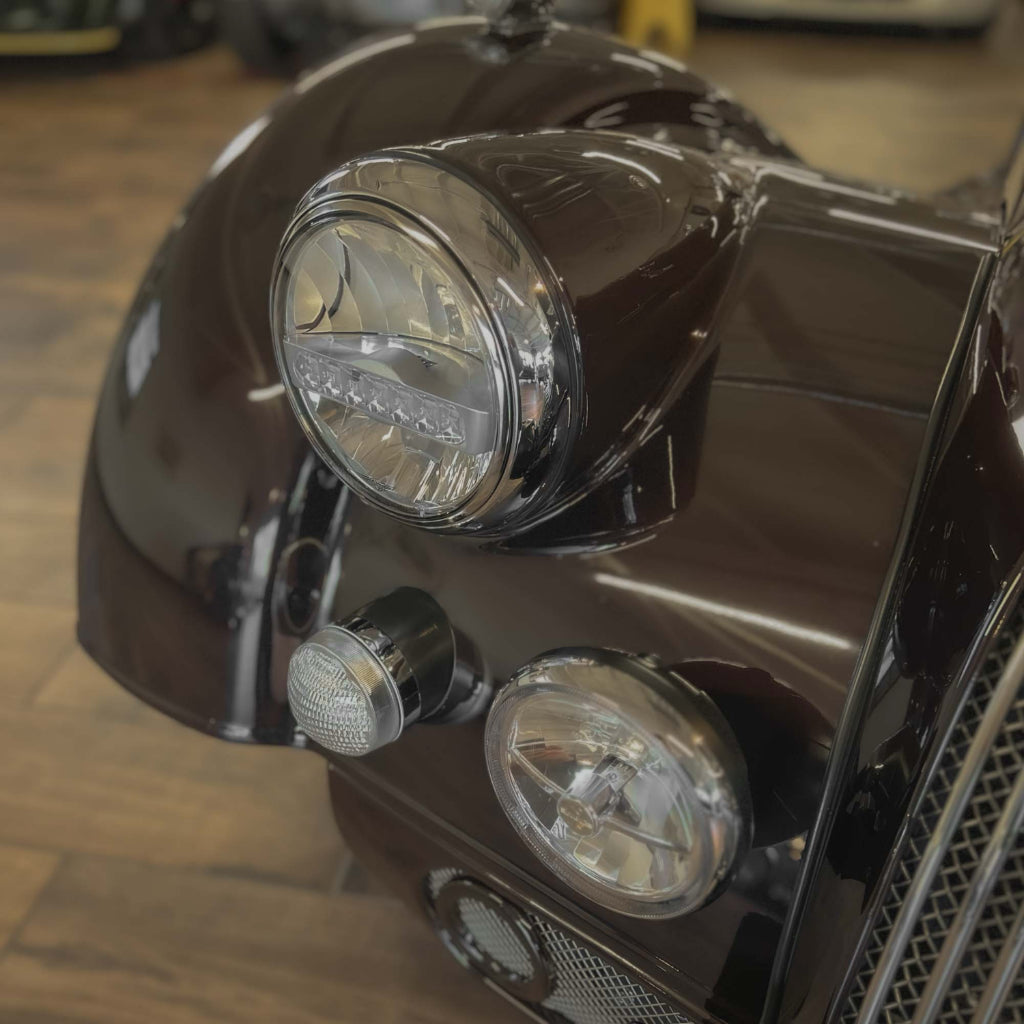Close-up of a car's front headlight and grille in a showroom setting