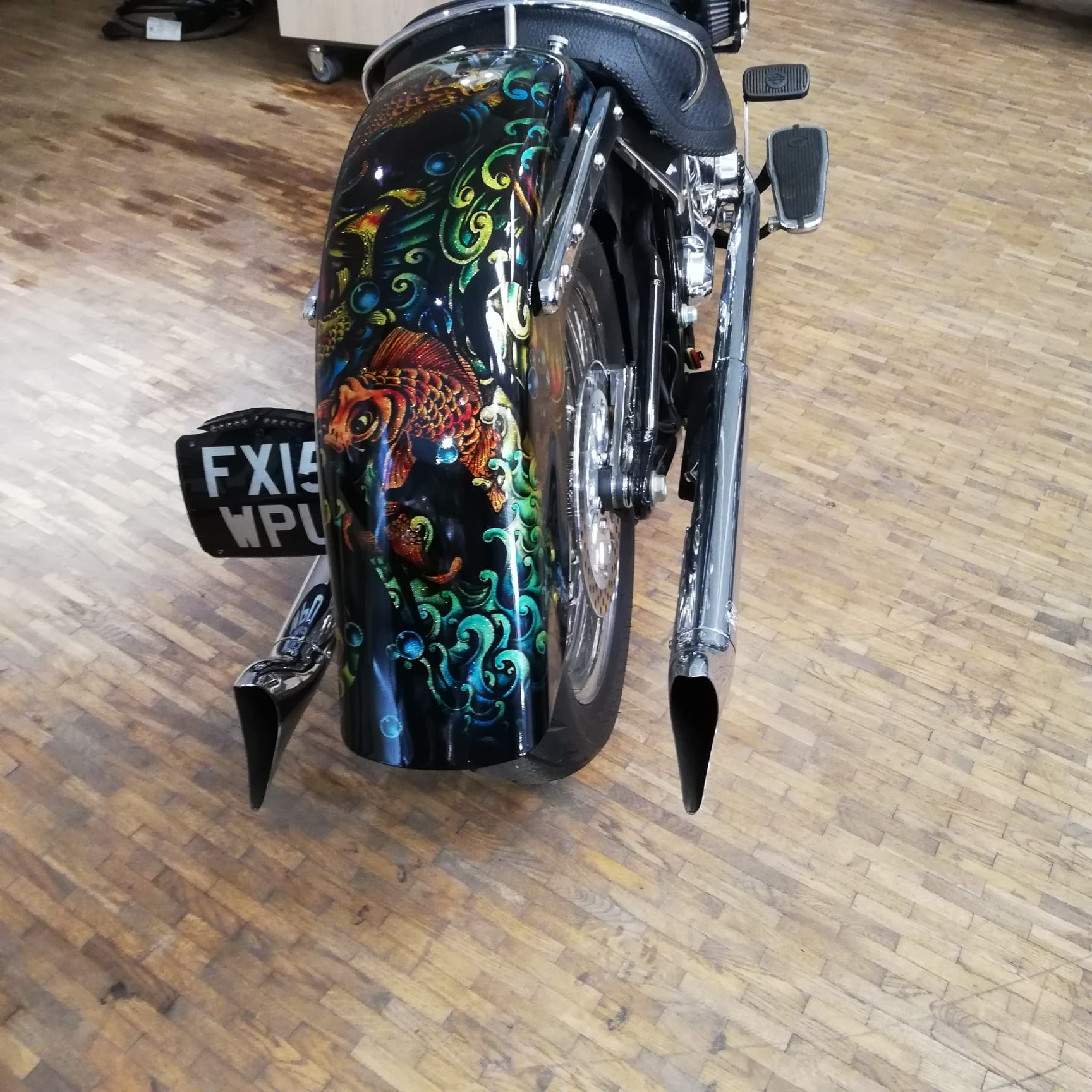 Motorcycle with a colorful design on the back tire on a wooden floor.