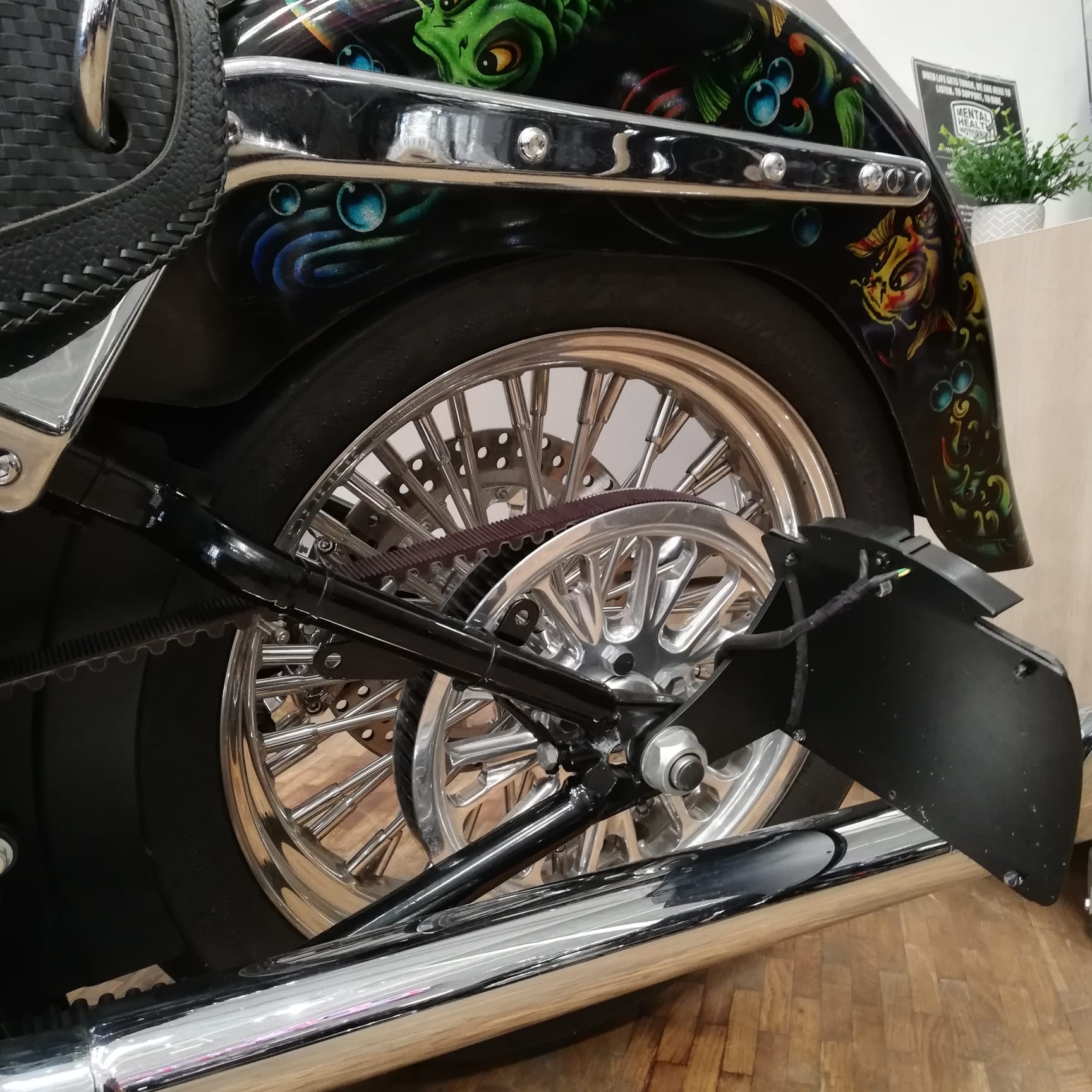 Close-up of a motorcycle wheel with decorative fender and colorful design on a wooden floor.