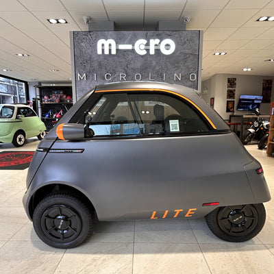 Microlino Lite electric car in a showroom with 'Micro' branding.
