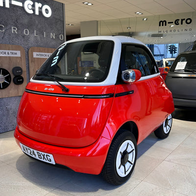 Small red car in a showroom with 'micro' branding.