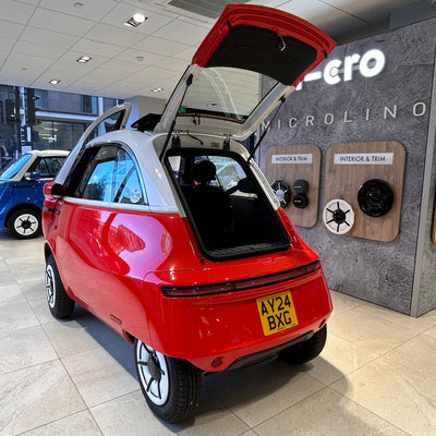 Red microcar with open hatch in a showroom setting