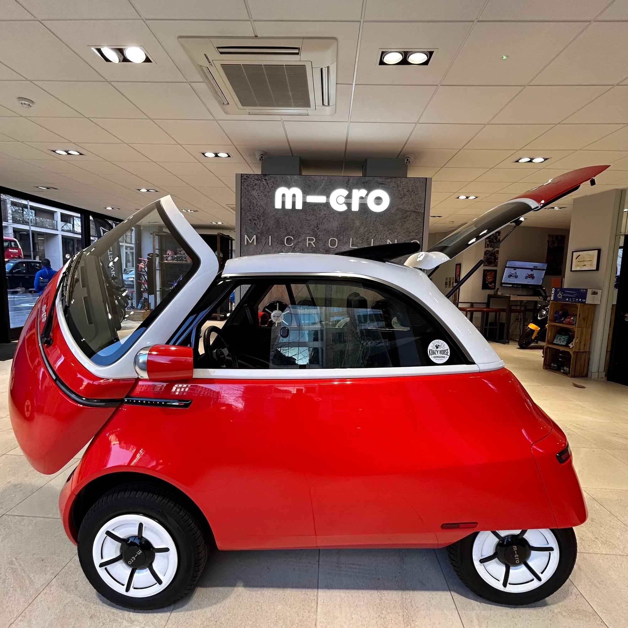 Red microcar on display in a showroom with 'm-ero' branding.