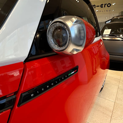 Close-up of a red car's headlight with 'Micro Ring' branding in a showroom setting.