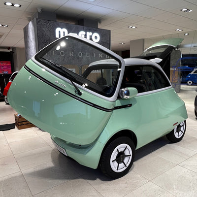 Small green car on display in a showroom with 'Micro' branding.