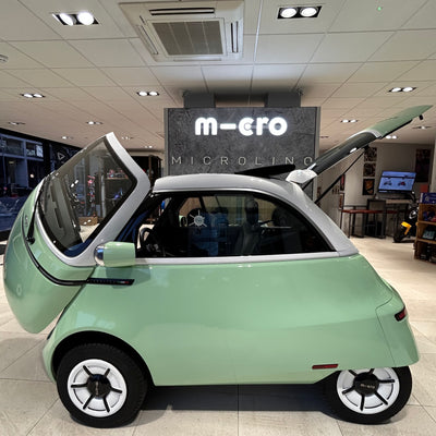 Small green car with open doors in a showroom setting, featuring the brand 'm-ero'.