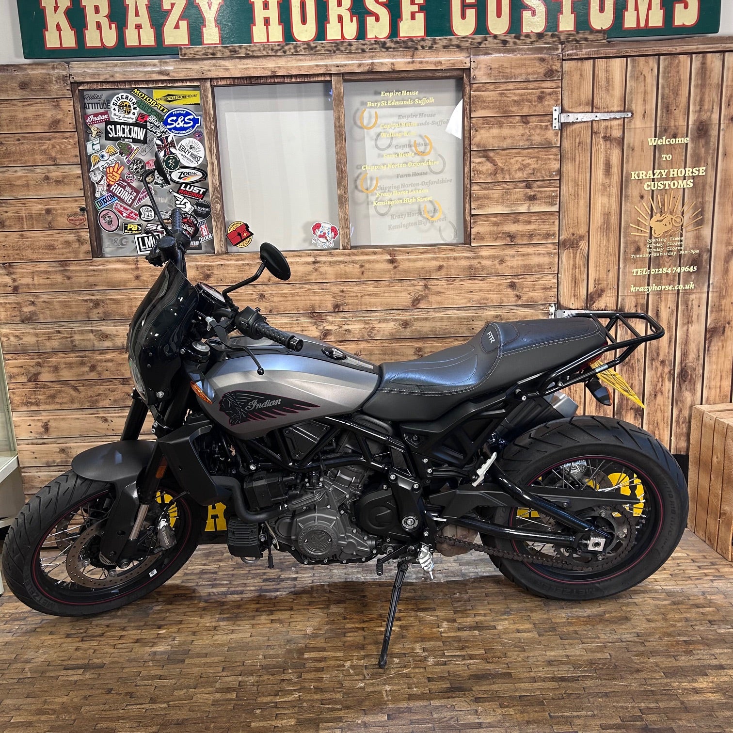 Motorcycle parked in front of a wooden wall with signs and posters.