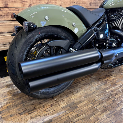 Close-up of a motorcycle with a focus on the exhaust system on a wooden floor.