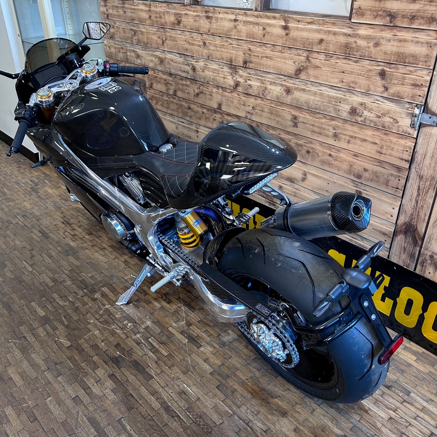 Black motorcycle parked indoors against a wooden wall.