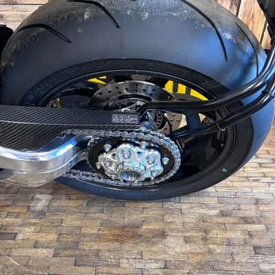 Close-up of a motorcycle tire and chain on a wooden floor