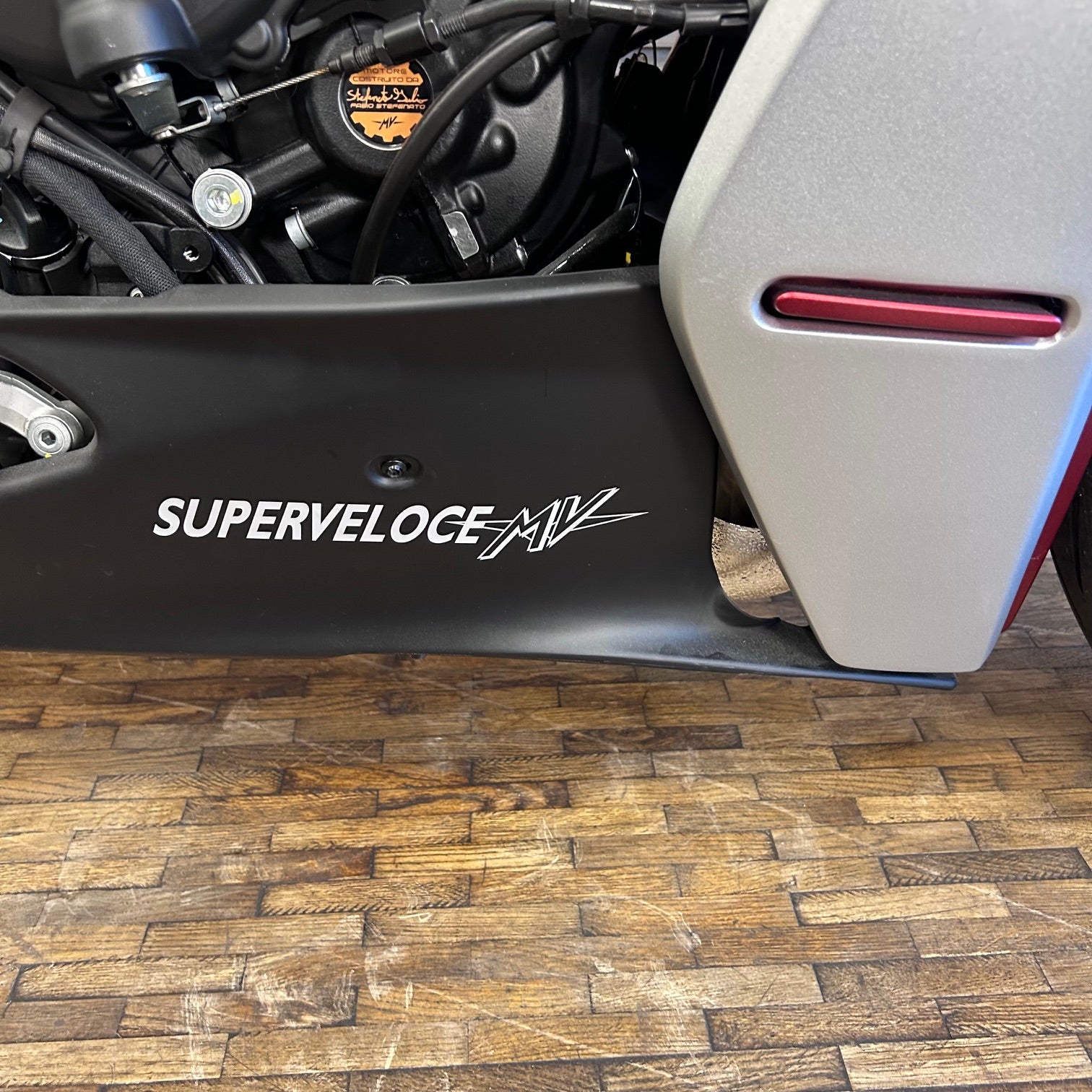 Close-up of a motorcycle with 'Superveloce MV' branding on a wooden floor.