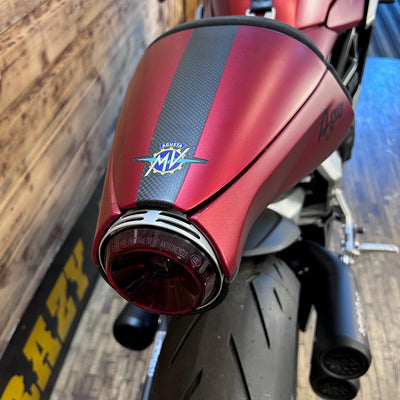 Close-up of a red motorcycle exhaust with MV Agusta logo against a wooden background