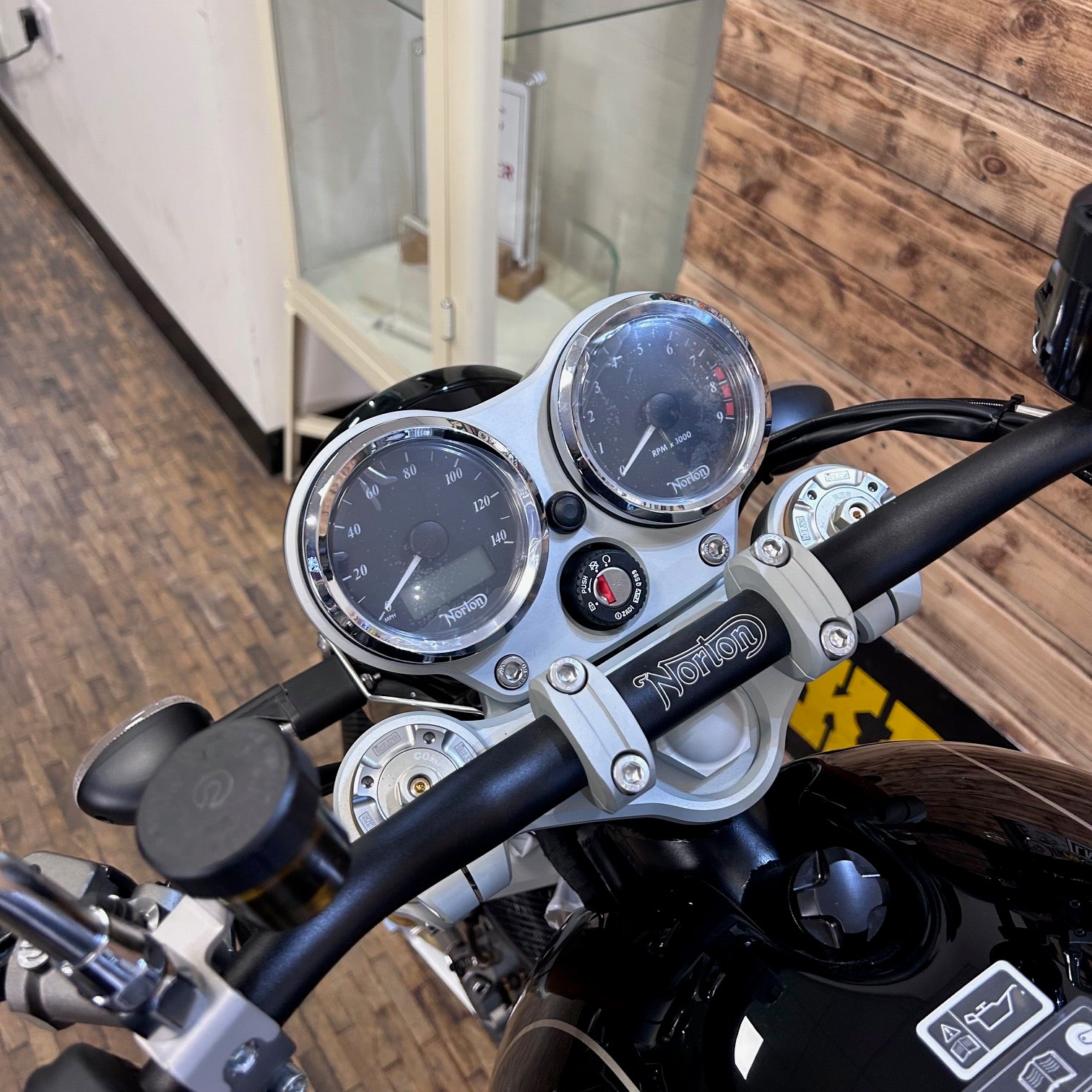 Motorcycle handlebar with gauges and Norton branding in a garage setting