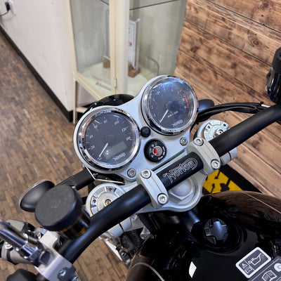 Motorcycle handlebar with gauges and Norton branding in a garage setting