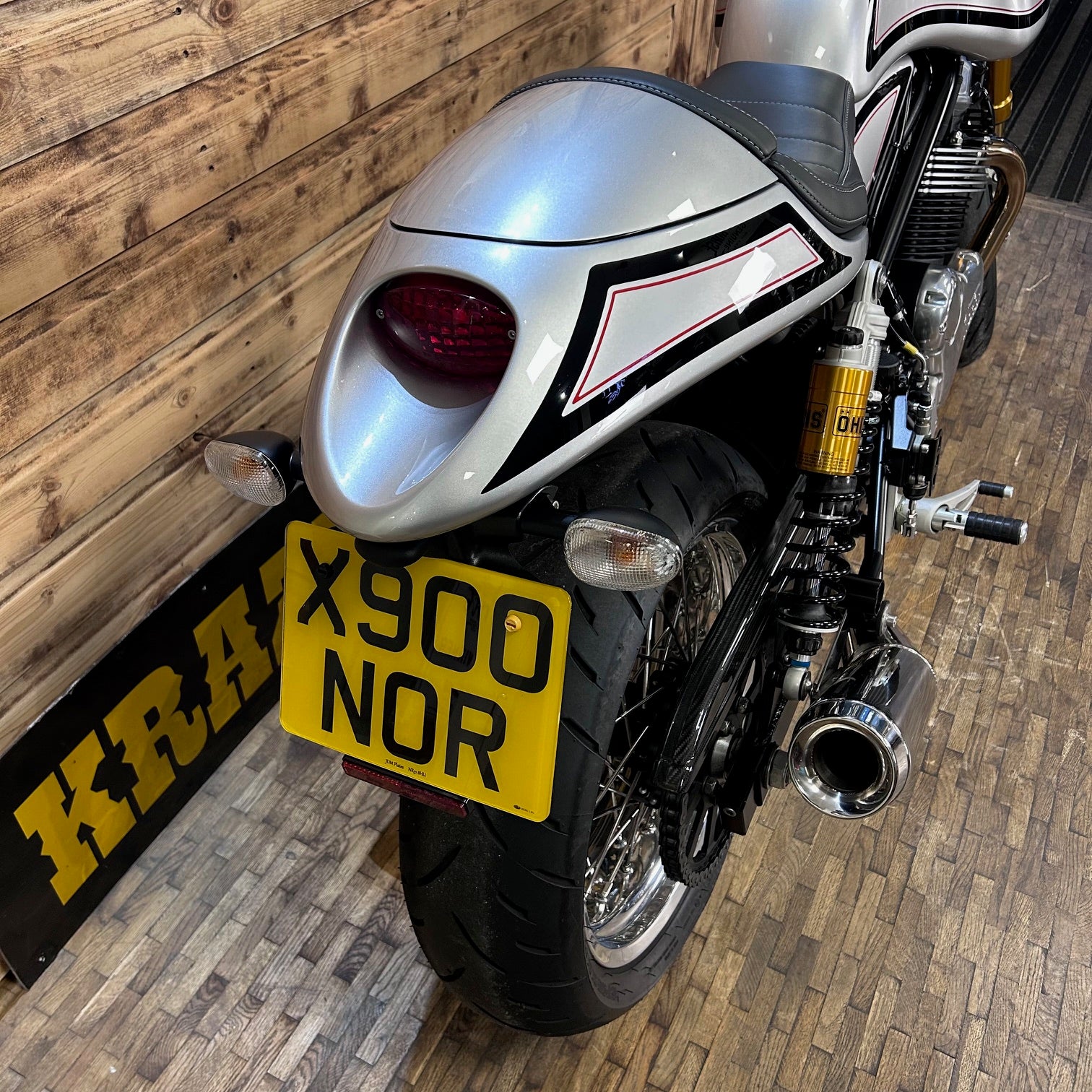 Motorcycle with a yellow license plate against a wooden wall.