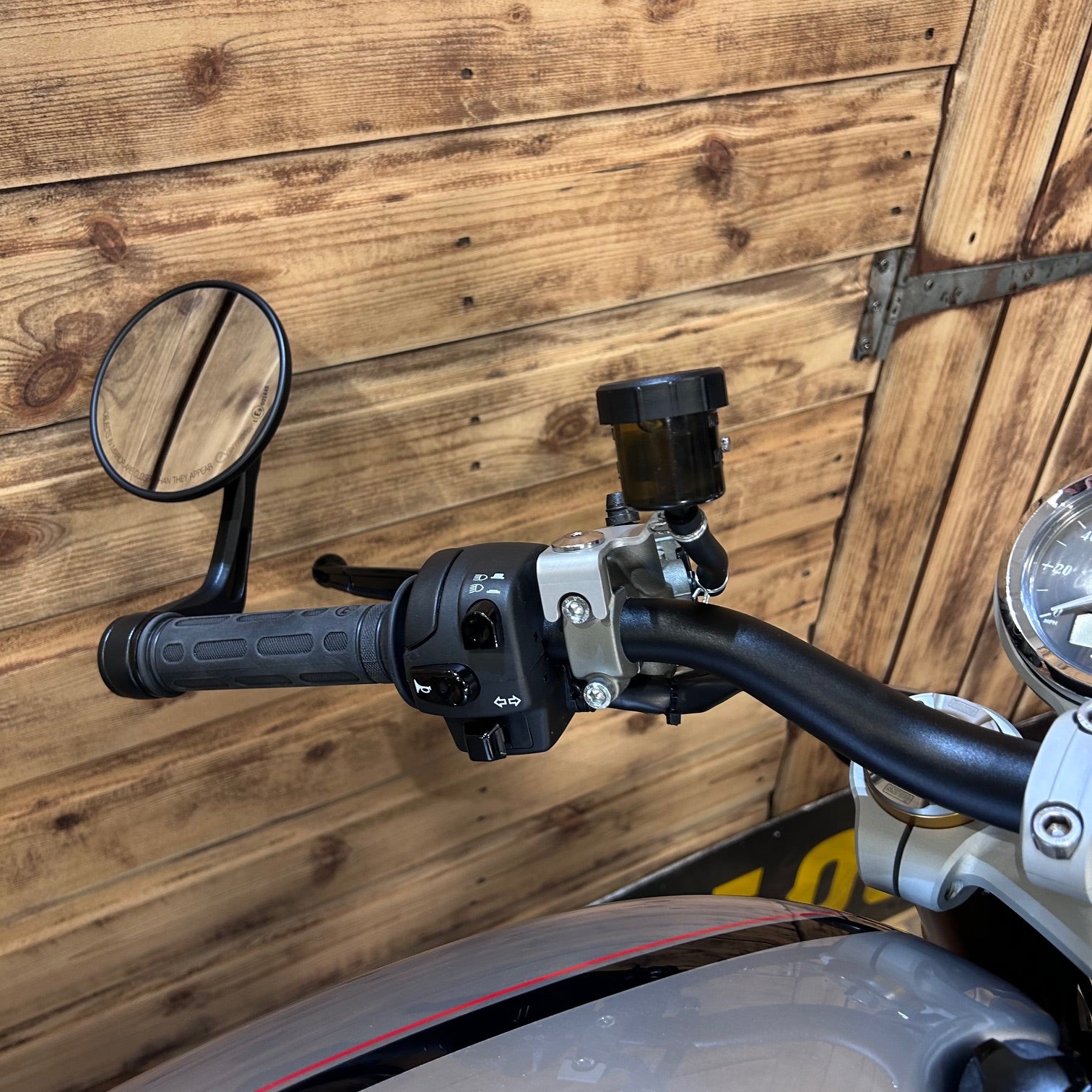 Close-up of motorcycle handlebar with mirror against a wooden wall