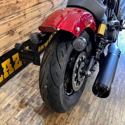 Close-up of a motorcycle's rear wheel and exhaust on a wooden floor.