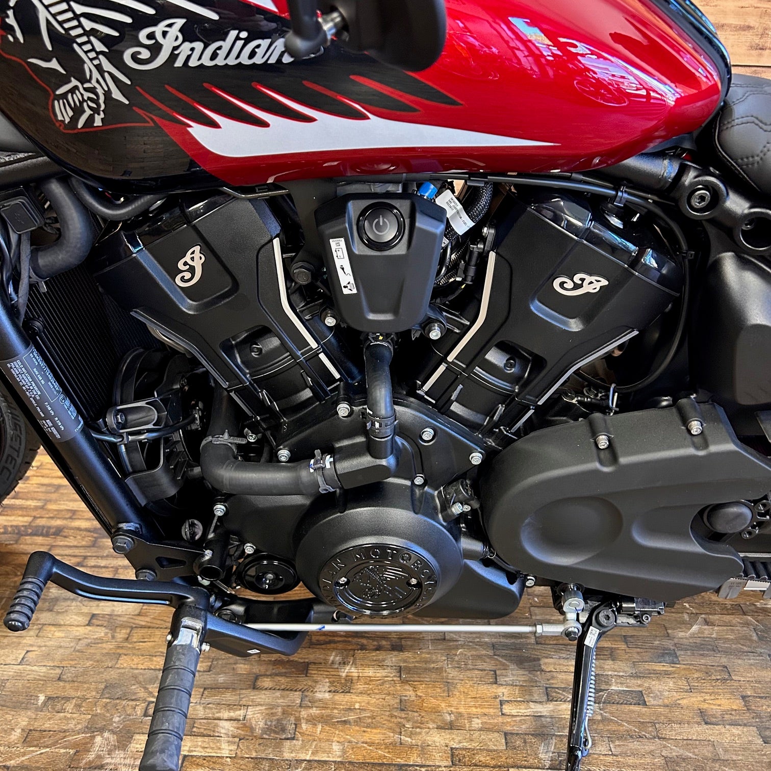 Close-up of a motorcycle engine with 'Indian' branding on a wooden floor.