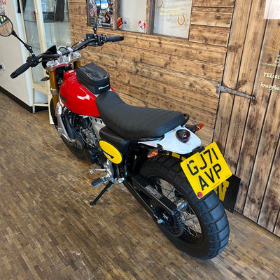 Red motorcycle with a yellow license plate on a wooden floor.