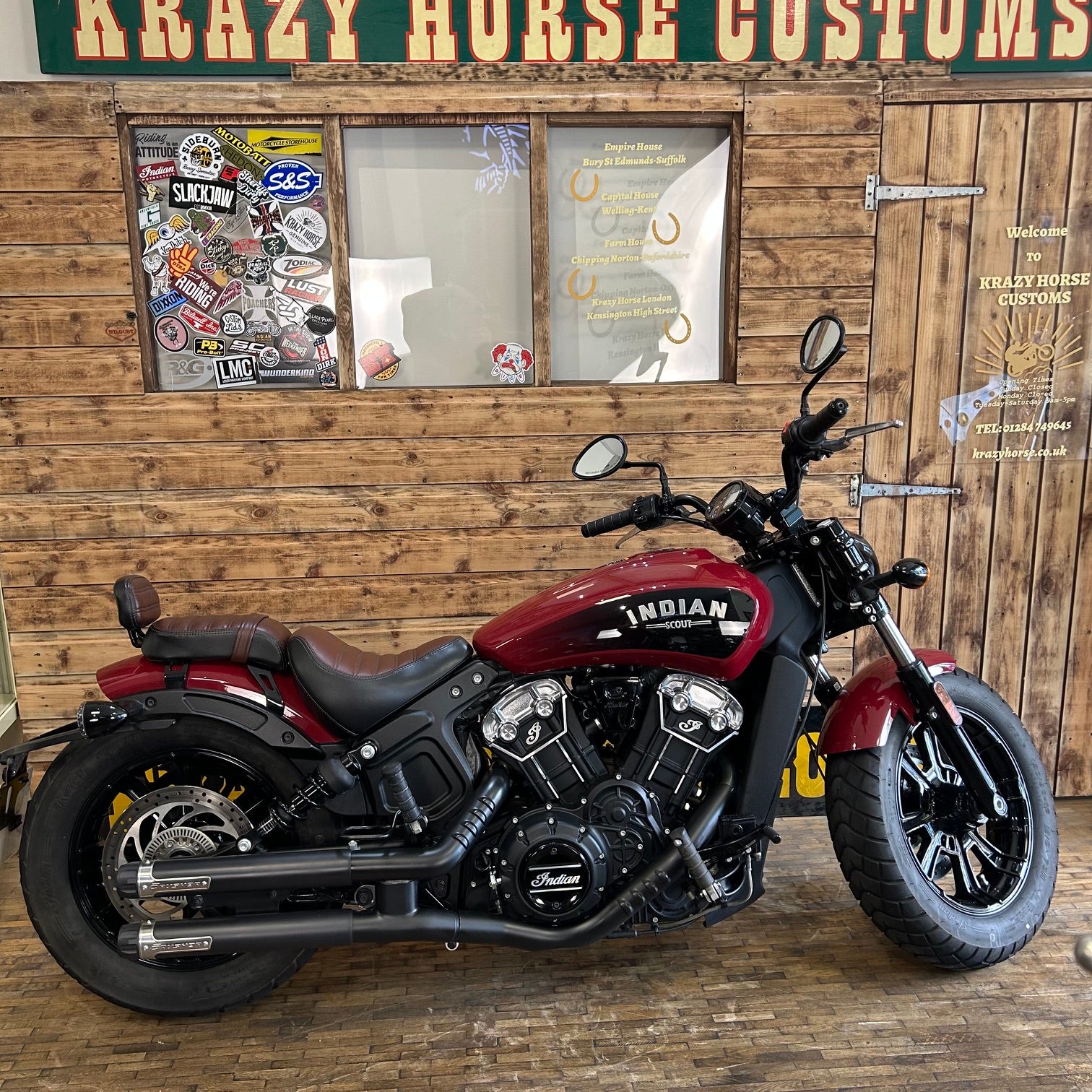 Red Indian motorcycle parked in front of a wooden wall with 'Krazy Horse Customs' sign.