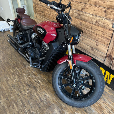 Red and black motorcycle parked indoors against a wooden wall.