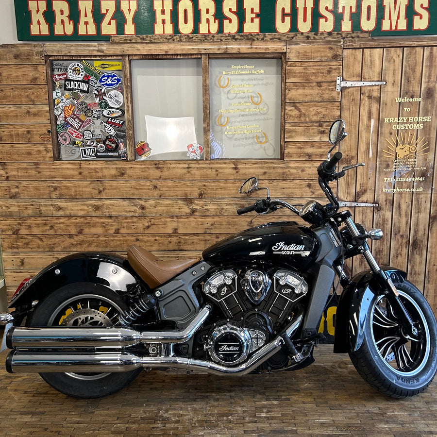 Black motorcycle with chrome details in front of a wooden wall with 'Krazy Horse Customs' sign.