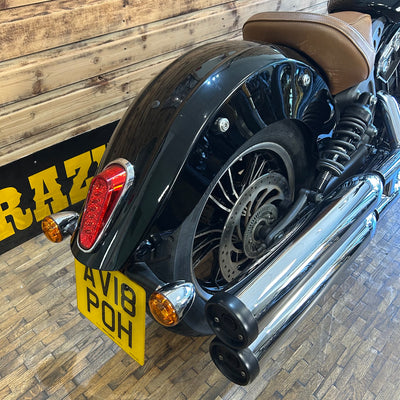Close-up of a motorcycle's rear section with a visible license plate on a wooden floor.